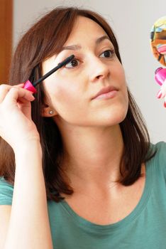 portrait of young caucasian brunette woman applying mascara on eyelashes