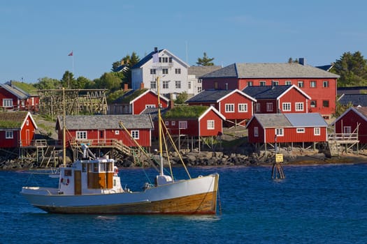 Red fishing rorbu huts and fishing boat in town of Reine on Lofoten islands