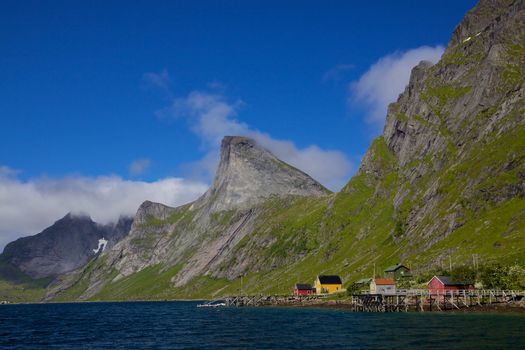 Picturesque fjord on Lofoten islands in Norway surrounded by towering mountain peaks and small fishing village