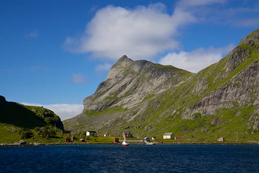 Picturesque fjord on Lofoten islands in Norway surrounded by towering mountain peaks and small fishing village