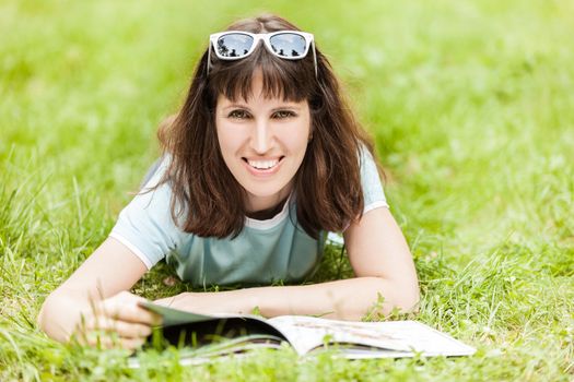 Beauty young smiling caucasian woman in sunglasses reading book outdoor on green grass field