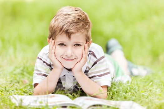Beauty smiling child boy reading book outdoor on green grass field