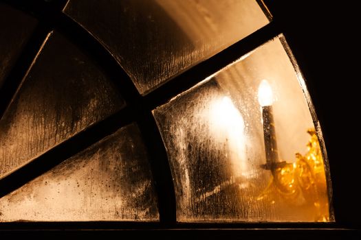 Glowing lamp light in stained arch window of old church