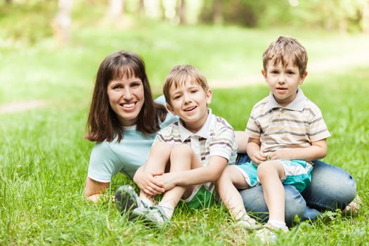 Beauty smiling mother and little sons walking outdoor on green grass field