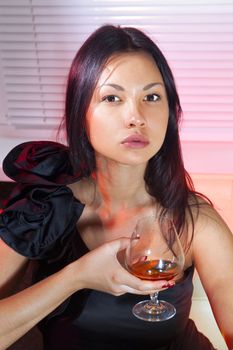 beautiful woman in black dress on sofa with glass of brandy