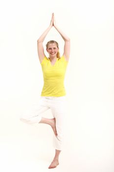 Fit attractve blonde woman practising yoga smiling happily as she balances on one foot with her arms raised above her head isolated on white