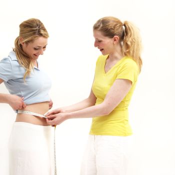 Smiling woman measuring her friends waist to confirm her achievemnt in losing weight isolated on white 