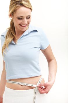 Elated woman measuring her waist smiling in joy at confirming her success in losing weight through dieting and exercise 