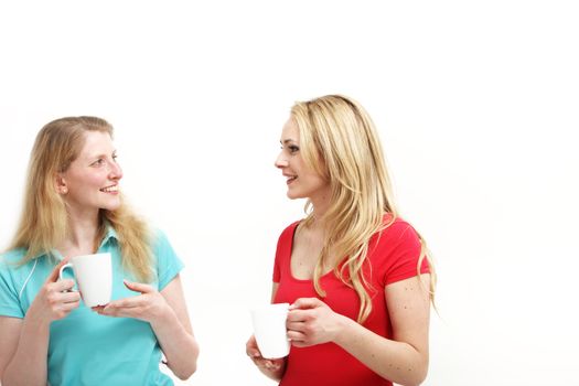 Two attractive young women standing chatting over a cup of coffee isolated on white 