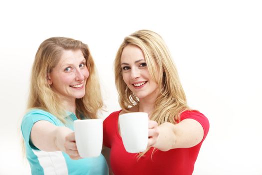 Two happy attractive women smiling in amusement raising their mugs and toasting with coffee isolated on white 
