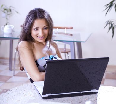 Young happy woman uses laptop computer in internet cafe