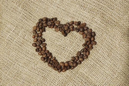 Closeup of coffee shaped heart on canvas. Heart of Coffee beans on macro. Arabic roasting coffee - ingredient of hot beverage.