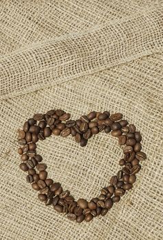 Heart of coffee beans on canvas. Closeup. Coffee beans on macro ground canvas background.