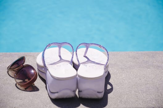 Women's flip flops and sunglasses by the swimming pool