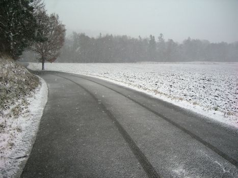           Lonely road in the winter country with a snow falling from the sky
