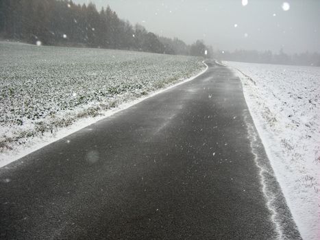           Lonely road in the winter country with a snow falling from the sky