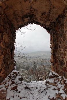 Look through an old caste ruin window at a forest covered by snow