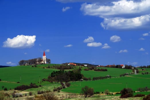Rural landscape with green fields, village and blue sky