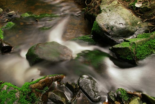 Hidden mountain brook with stones and moss with long exposure