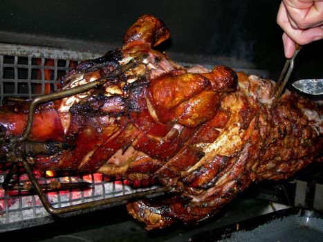           Hand of a man is cutting slices of the pig on the grill