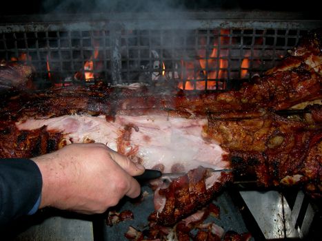           Hand of a man is cutting slices of the pig on the grill          