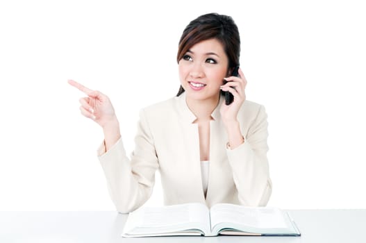 Portrait of an attractive young Asian businesswoman talking on mobile phone and pointing at copy space over white background.