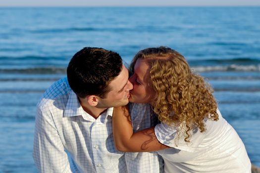 A young couple a standing near beach kissing.