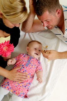 Mother and father are looking and playing with their sweet smiling 4 month old baby.