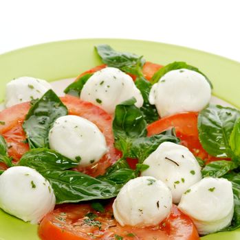 Italian Caprese Salad with Basil, Fresh Mozzarella, Tomatoes and Olive Oil on green plate close up on white background
