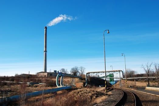 Industrial plant with pipes leading to chimney and railroad
