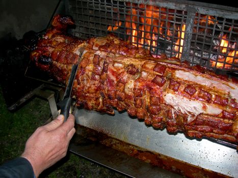           Hand of a man is cutting slices of the pig on the grill