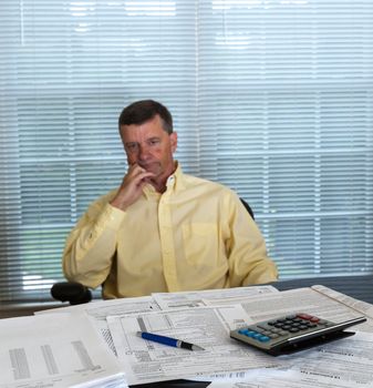 Senior caucasian man weary from preparing tax form 1040 for tax year 2012  with calculator