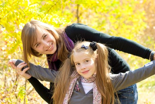 Smiling young mother with little daughter outdoor. Autumn day.