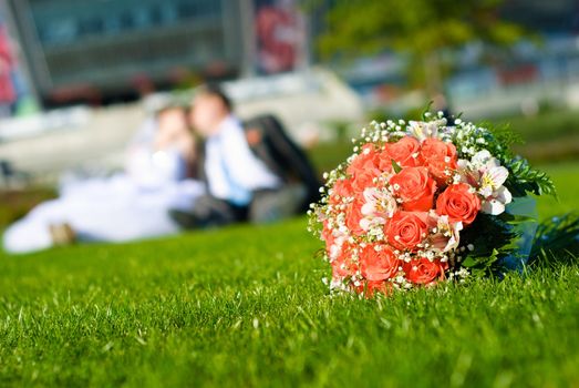 Bridal bouquet of red roses on a green meadow and blurred newlyweds