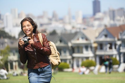 Alamo Square San Francisco Tourist. Young traveler woman holding camera taking tourist photo in Alamo Park by the Painted Ladies, The Seven Sisters, San Francisco, California, USA. Beautiful happy smiling multicultural woman.