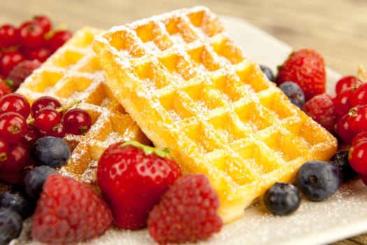 fresh tasty waffer with powder sugar and mixed fruits on wooden background