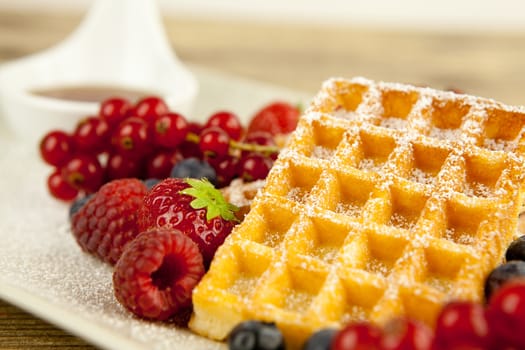 fresh tasty waffer with powder sugar and mixed fruits on wooden background