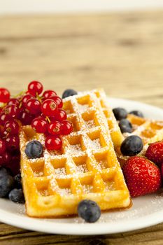 fresh tasty waffer with powder sugar and mixed fruits on wooden background