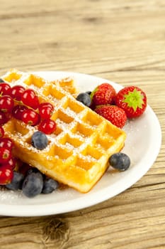 fresh tasty waffer with powder sugar and mixed fruits on wooden background