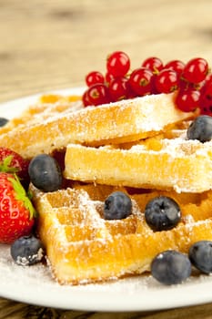 fresh tasty waffer with powder sugar and mixed fruits on wooden background
