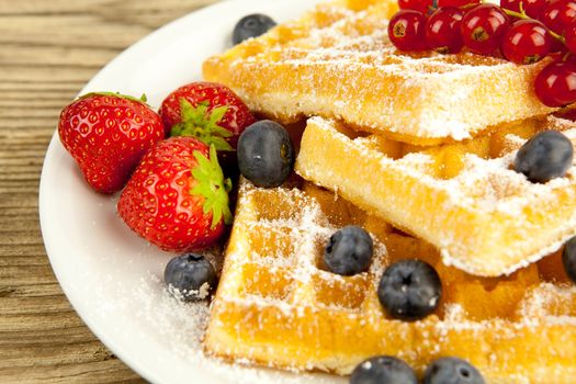 fresh tasty waffer with powder sugar and mixed fruits on wooden background