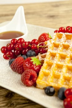 fresh tasty waffer with powder sugar and mixed fruits on wooden background