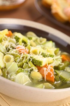 Bowl full of fresh homemade vegetarian Italian minestrone soup made of green beans, zucchini, carrots, potatoes, leek and shell pasta with grated cheese on top (Selective Focus, Focus one third into the soup)