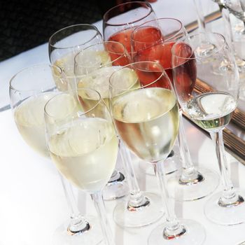 Wine glasses filled with chilled white and rose wine on a buffet table at a catered event 