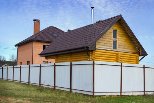 Brick house and wooden house behind a high fence