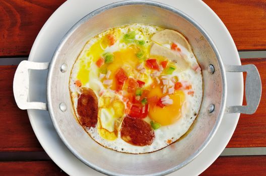Fried egg with Chinese sausage in pan on wooden table