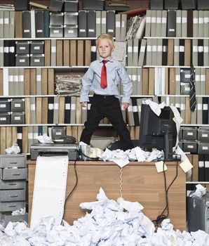 Young businessman standing on the table in a messy office