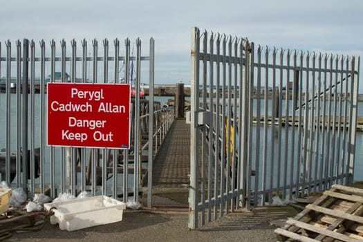 A fisherman's dock security gates with a gangway, a sign on the railings with the words 'Danger Keep Out'.