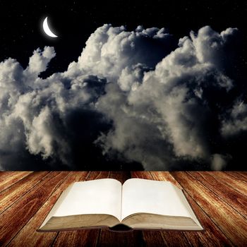 Open blak book on wooden table with night sky