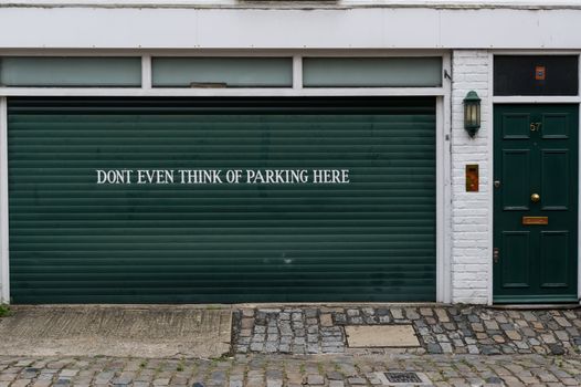 Garage sign prohibiting parking painted on the door of a private garage saying "Dont even think of parking here"